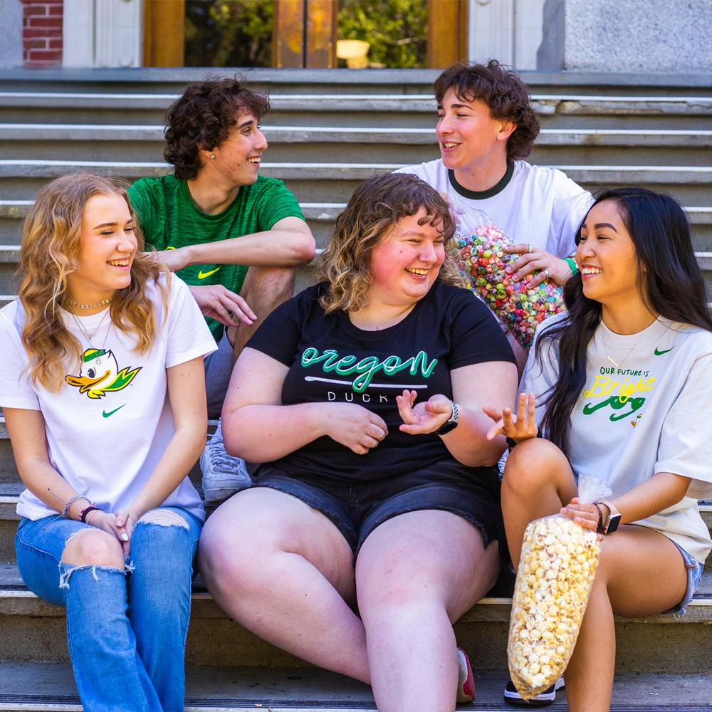 A group of University of Oregon students posing for a photo at the Street Faire eating popcorn on steps.