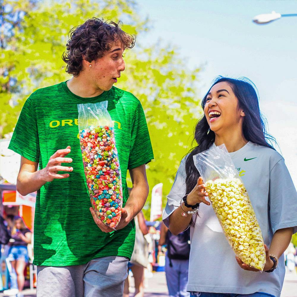 Two University of Oregon students posing for a photo at the Street Faire, eating popcorn.